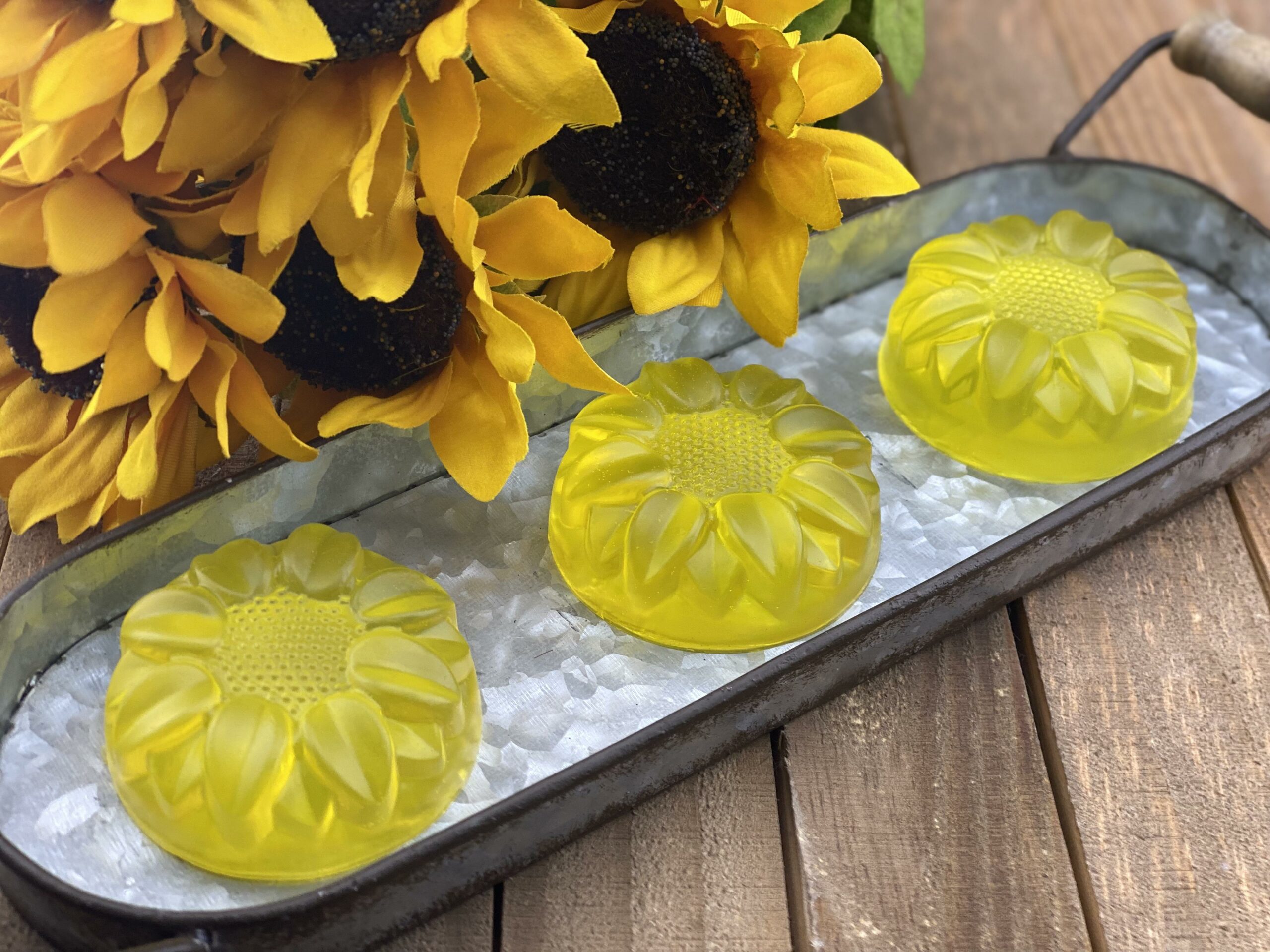 3 yellow sunflower molded soap in tin tray with sunflowers and wooden background